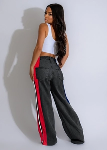 Detail shot of black denim pants featuring bold red and white side stripe contrast panels