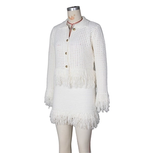Detail of white crochet knit cardigan and mini skirt set with gold buttons and fringe trim