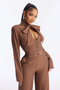 Detail of brown pinstripe jumpsuit showing halter neck bow, V-cutout, and decorative buttons