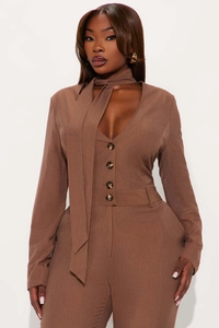 Detail of brown pinstripe jumpsuit featuring resin buttons and stylish neck tie