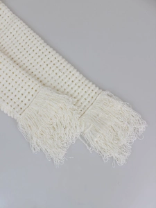 Close-up of cream knit fabric showing open mesh texture and long fringe detail tassels