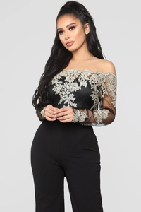 Detail of gold floral lace embroidery on black off-the-shoulder jumpsuit with sheer sleeves