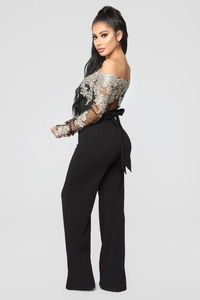 Detail of off-shoulder black jumpsuit featuring floral lace embroidery and waist tie
