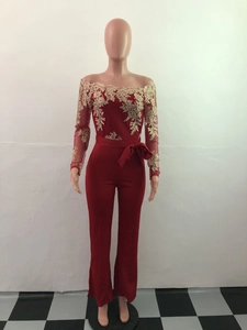Close-up of red off-shoulder jumpsuit with gold lace embroidery and waist tie bow