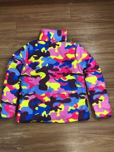 Flat lay of unisex puffer jacket with colorful camouflage pattern on wooden floor background