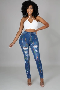Dettaglio di jeans blu slim fit con schizzi di vernice colorati e trame strappate sulle ginocchia