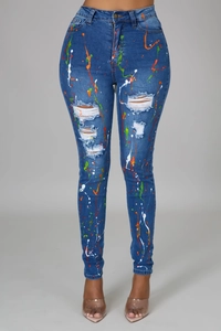 Dettaglio dei jeans skinny a vita alta con strappi sulle ginocchia e schizzi di colore