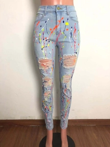 Dettaglio dei jeans skinny azzurri con schizzi di colore vivaci e strappi usurati sulle ginocchia