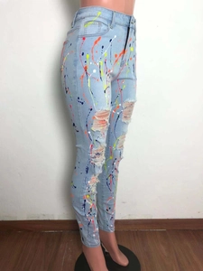 Dettaglio jeans blu chiaro con schizzi di vernice colorati e strappi sulle ginocchia