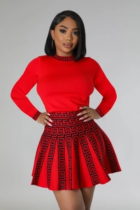 Detail of red knit two-piece set with long sleeve top and pleated skirt featuring greca trim