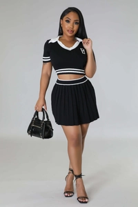 Detail of a two-piece black knit set with a cropped polo top and pleated mini skirt