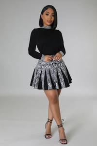 Detailed view of the contrast Greek key pattern on black pleated knit dress hem