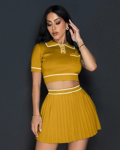 Detail of ginger yellow knitted polo crop top and pleated skirt with white contrast trim