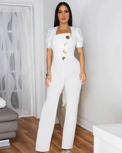 Detail showing white slim fit jumpsuit with gold relief buttons and asymmetric square neck