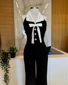 Details des monochromen Neckholder-Jumpsuits mit weißer Schleife und Strassknöpfen