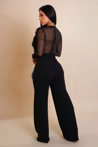 Detail view of women's black jumpsuit featuring sheer mesh panels and elegant ruffle trim