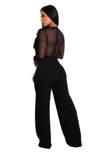 Detail of sheer mesh paneling and ruffle accents on a black high-waisted wide-leg jumpsuit
