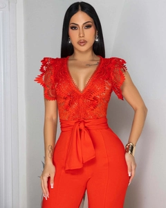 Detailed view of red jumpsuit featuring delicate lace cutouts and deep V-neckline texture