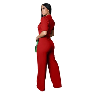 Rear side view of red short sleeve wide leg jumpsuit with waist tie and green handbag