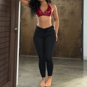 Détail d'un jean skinny noir taille haute porté avec un haut licou en similicuir rouge