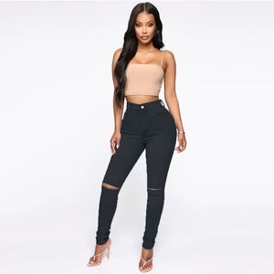 Detail of high-waist black skinny jeans with ripped knee design and elastic denim fabric