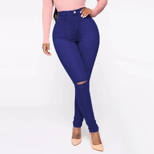 Detail of high waist skinny blue jeans featuring a stylish distressed hole on the left knee