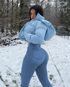 Détail d'une doudoune bleue avec logo et d'un jean slim taille haute en paysage de neige