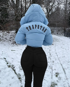 Sky blue hooded puffer jacket with black Trapstar gothic logo print on the back in snow