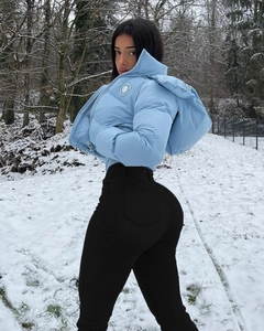 Détail de la doudoune à capuche bleu clair et du pantalon slim noir dans un décor de neige