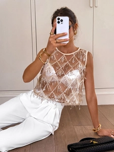 Détail de sequins dorés en losanges et longues franges sur un gilet de fête en maille