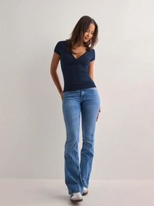 Detailed view of women's V-neck wrap top in navy blue with high-waist flared denim jeans