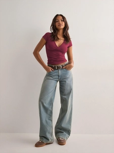 Detail of slim-fit wine red V-neck T-shirt paired with light blue wide-leg denim jeans