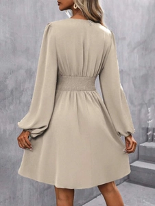 Detail view of the elastic pleated waist and A-line hem on this beige long sleeve dress