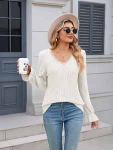Detail of ribbed knit texture with V-neck lace trim and ruffled cuffs on a long sleeve top