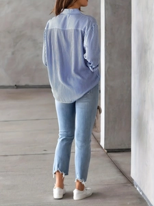 Rear view of a casual blue striped long sleeve shirt with curved hem and frayed jeans