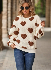 Détail d'un sweat en polaire blanche à motifs de cœurs marron et poignets côtelés