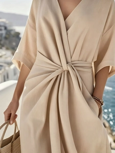 Detail of light beige V-neck dress featuring elegant waist tie and pleated texture fabric