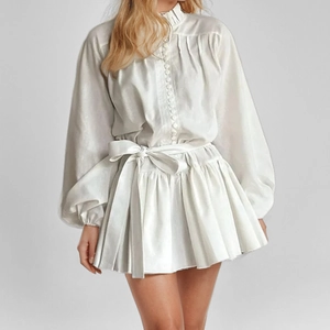 Detail of white long-sleeve mini dress with ruffles, lantern sleeves and waist bow tie