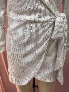 Macro shot of white sequin fabric and waist tie detail on a long-sleeve evening gown