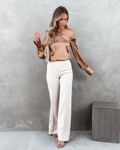 Detail of champagne satin one-shoulder blouse with asymmetric neckline and glossy texture