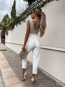 Detailed view of women's beige sleeveless top with scalloped back and white high-waist pants