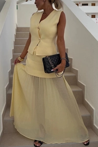 Dettaglio del gilet in maglia giallo chiaro con bottoni e gonna in tulle a pieghe