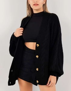 Détail de la maille torsadée épaisse et des boutons ambre sur un cardigan noir femme