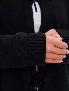 Detail of ribbed cuffs on a black chunky knit cardigan for women with textured fabric