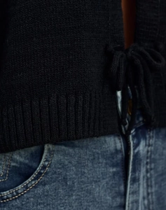 Detail of black knit cardigan showing ribbed hem and lace-up closure on the front side