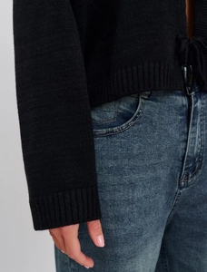 Close-up of black knit sweater ribbing texture and tie-neck detail with blue denim