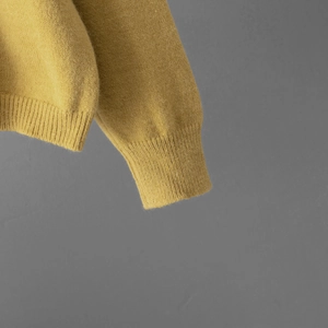 Gros plan d'un pull en maille jaune gingembre montrant la texture des poignets et du bas