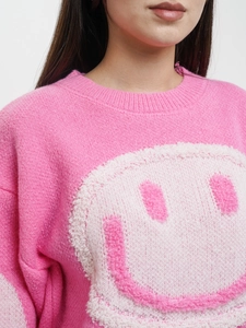 Detail of pink knitted sweater featuring a textured 3D smile graphic and ribbed neckline