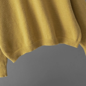 Gros plan du pull en maille jaune gingembre montrant l'ourlet côtelé et les poignets