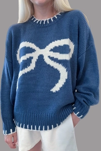 Detail of navy knit sweater featuring white bow pattern and decorative contrast stitching